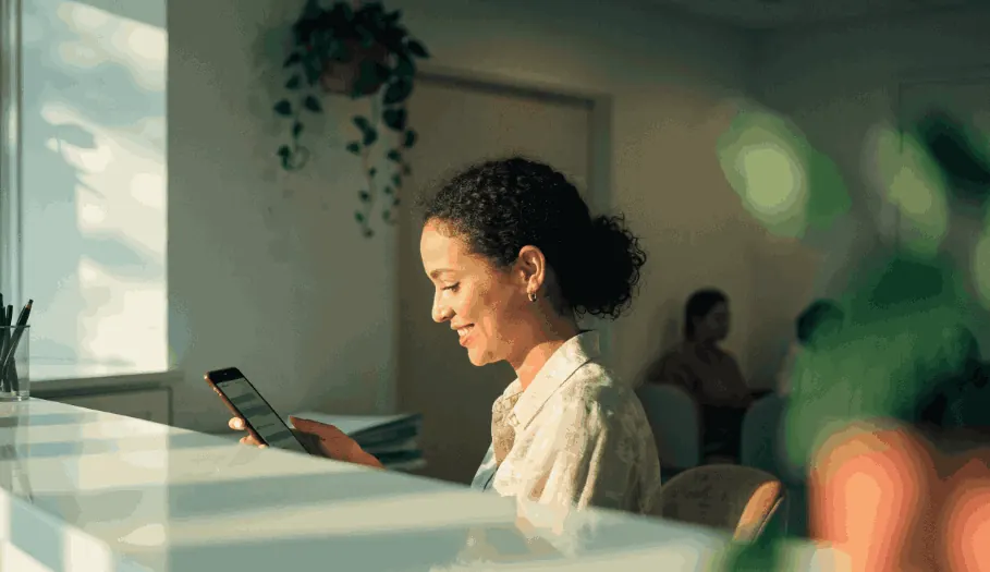 Recepcionista de clínica sorrindo com o celular na mão